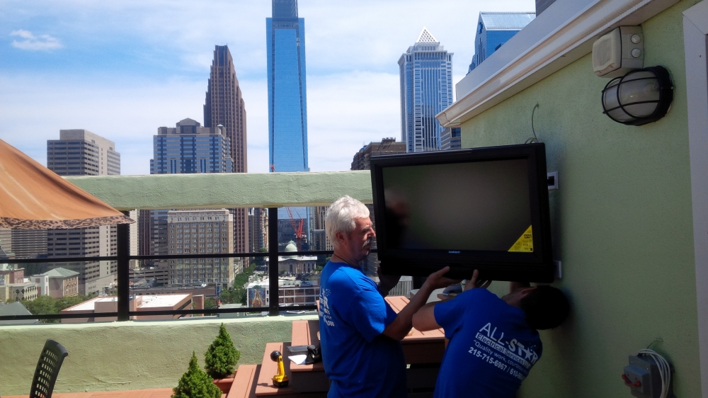 A technician from All Star Electrical Services, LLC installing an outdoor wall-mounted television