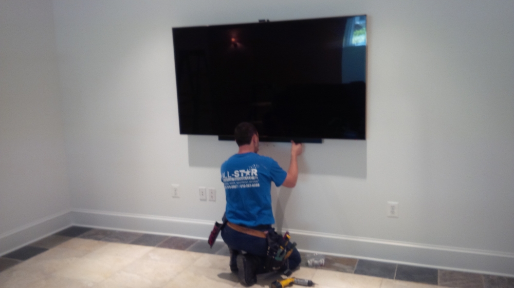A technician from All Star Electrical Services, LLC installing a large wall-mounted television