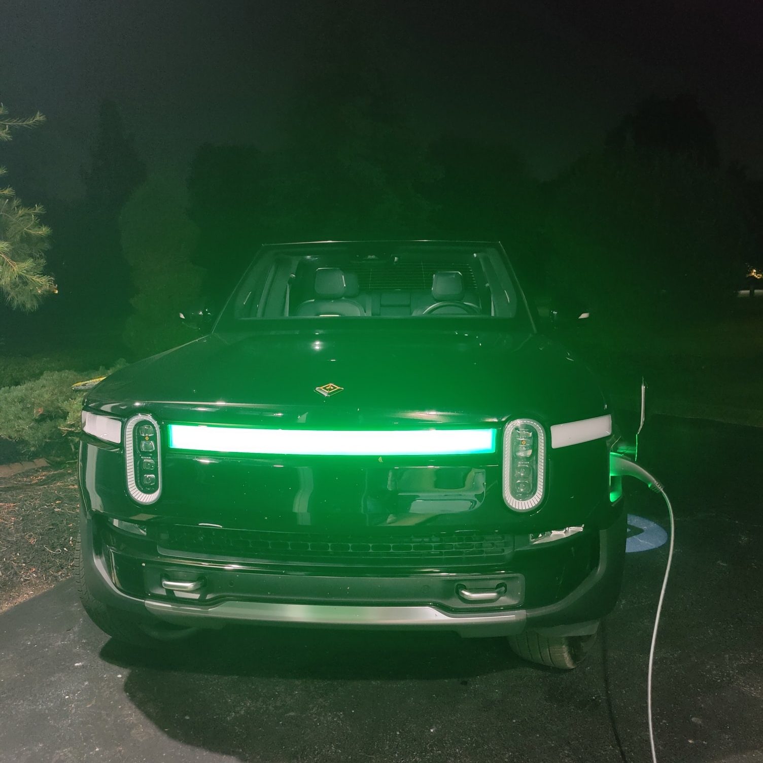 An electric vehicle, plugged in anc charging with a green light glowing in the front